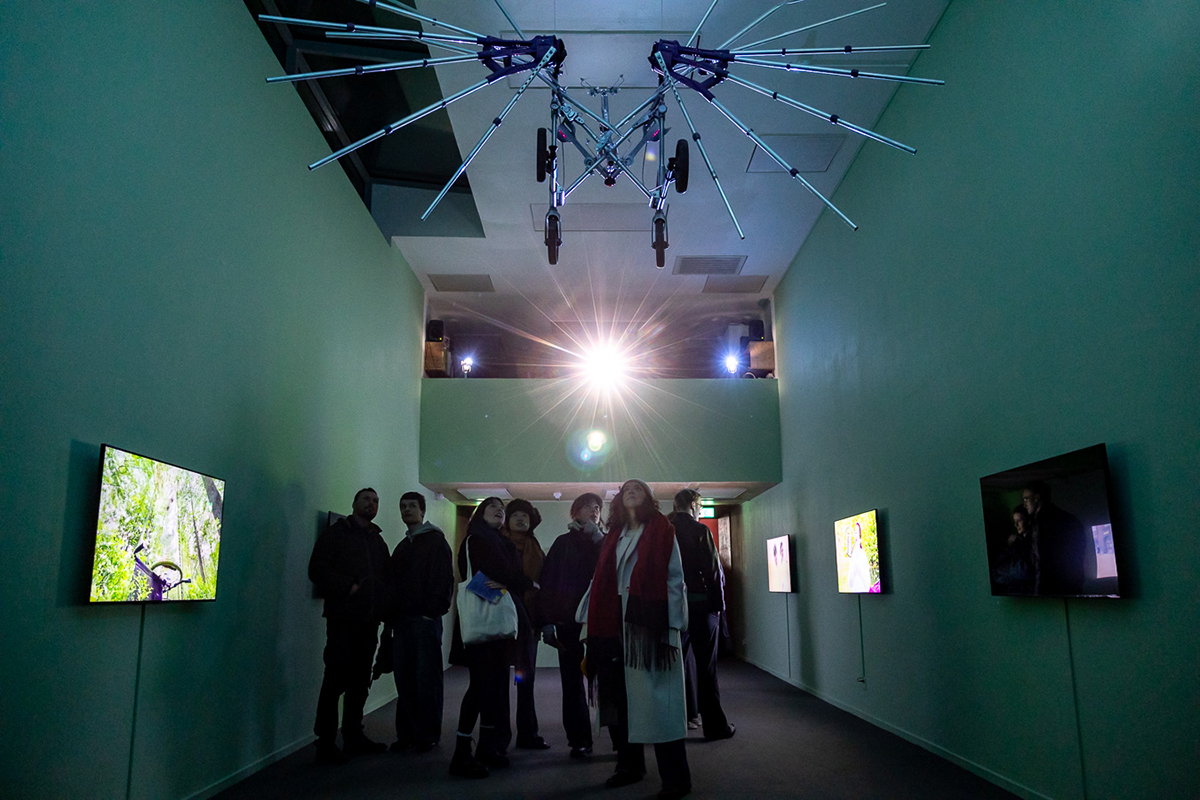 Audience is watching a walker with crutch wings in the ceiling of the gallery.