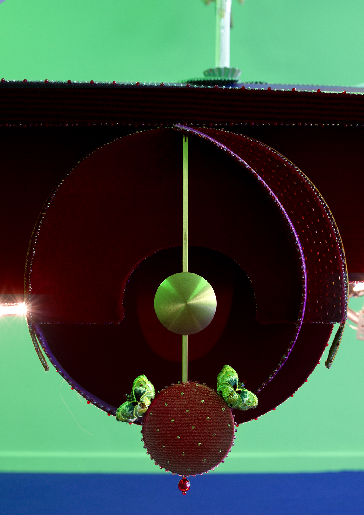 The car’s front wheels, made of red velvet, float in the air, and a wall clock weight hangs at their center.