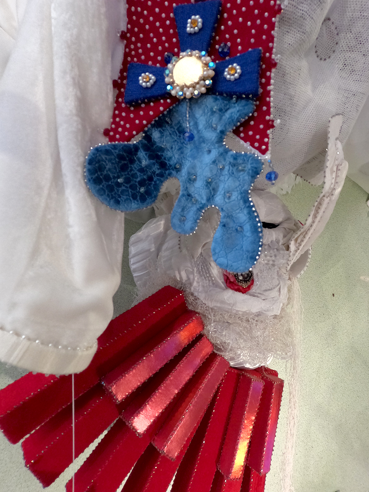 Character hiding inside a white laboratory coat. Tears stream upward towards the sky. In place of hair are red piano keys, resembling Venetian park benches. In the chest is a tearing medal.
