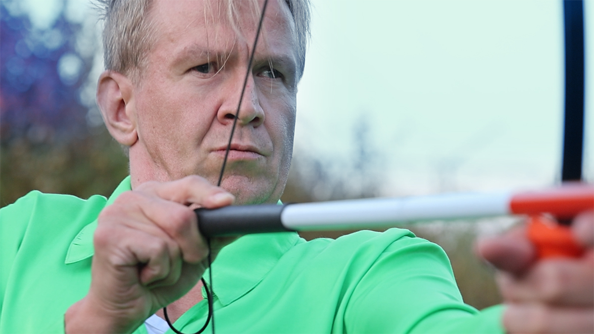 A blind man in a green silk shirt shoots white canes with a bow.