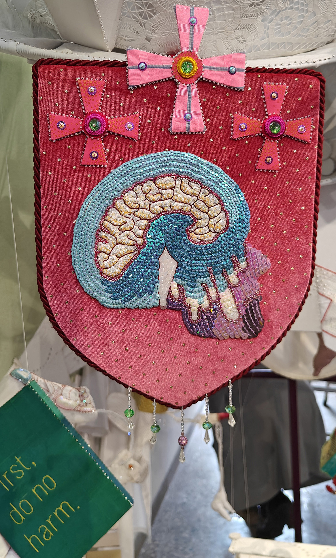 Coat of Arms with an image of lobotomy made of sequins. Under is a green book with silk covers and embroidered text: First Do No Harm.