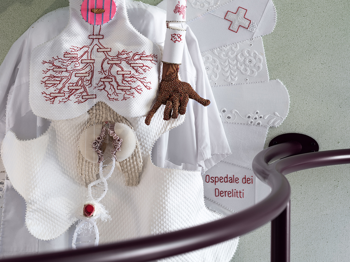 White textile figure on the wall. Instead of lungs there is an empty family tree upside down. From the pelvis comes out the DNA chain with a red lipstick at the end.